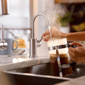 Person using a French press on a kitchen counter with a sink and coffee mug in the background.