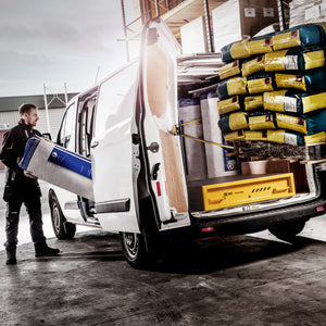 Person loading a large blue and white container into a van with various items loaded inside.