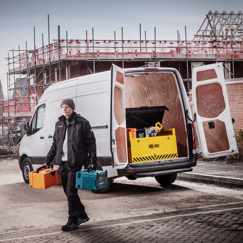 Person with tools walking towards a white van with open doors at a construction site.