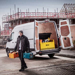 Person with tools walking towards a white van with open doors at a construction site.