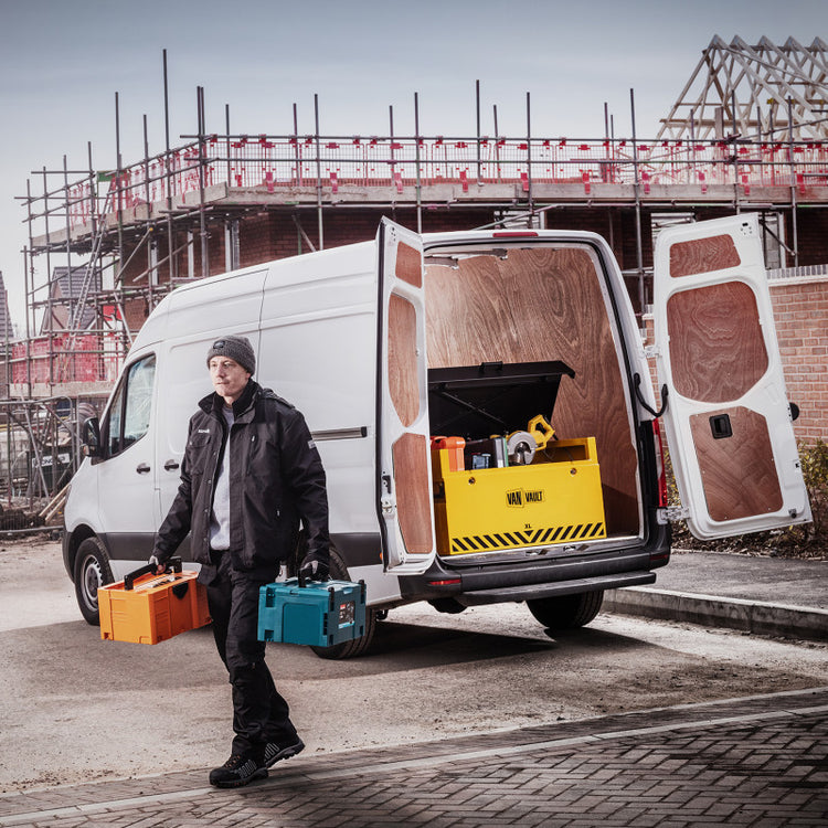 Person with tools walking towards a white van with open doors at a construction site.