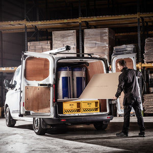 Person loading a white van with boxes and containers in a warehouse setting