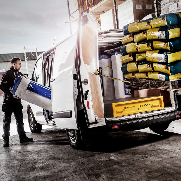 Person loading a large blue and white container into a van with various items loaded inside.